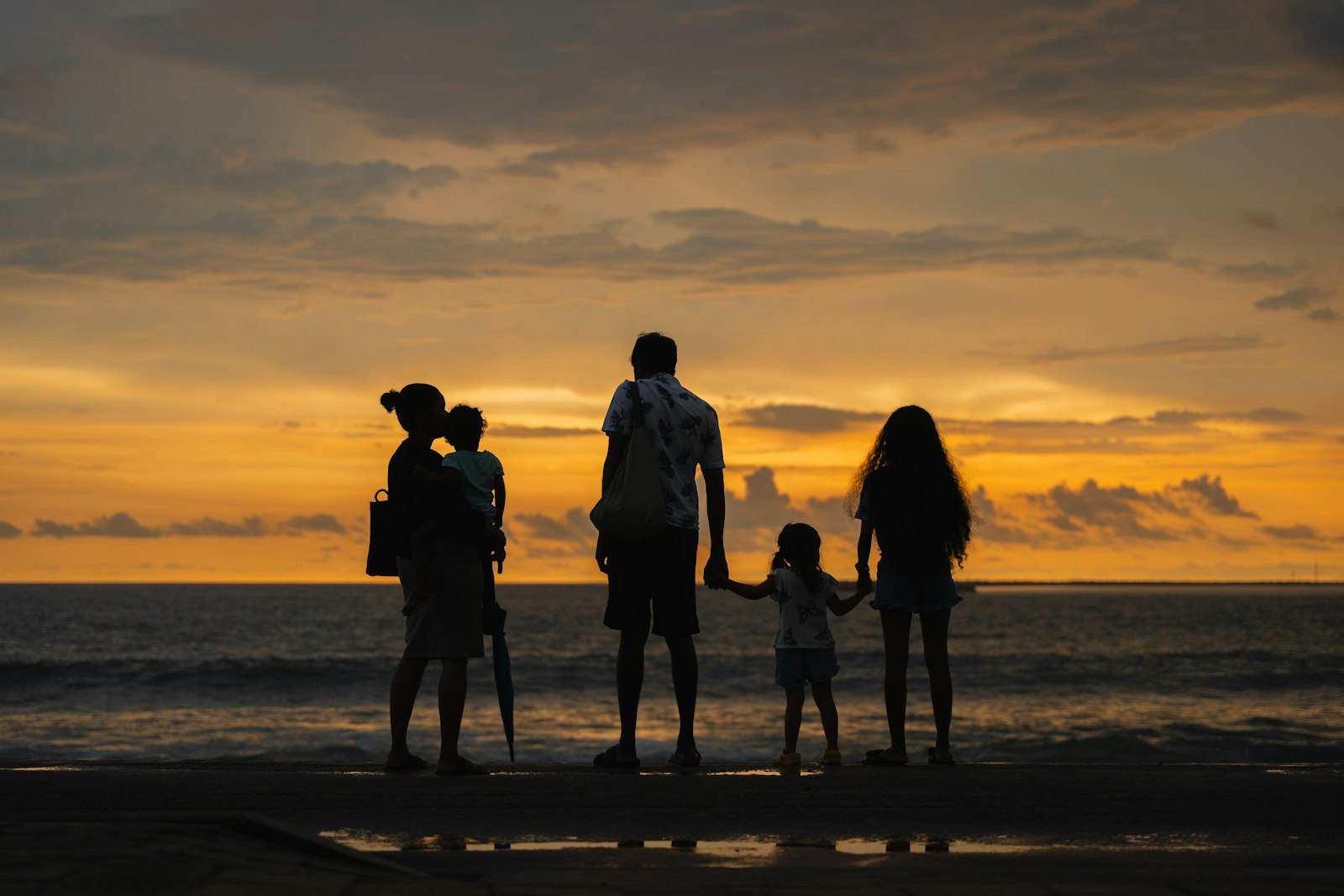 A family holding hands on the beach, looking out at the ocean at sunset